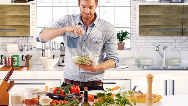 Handsome man cooking at home preparing salad in kitchen.